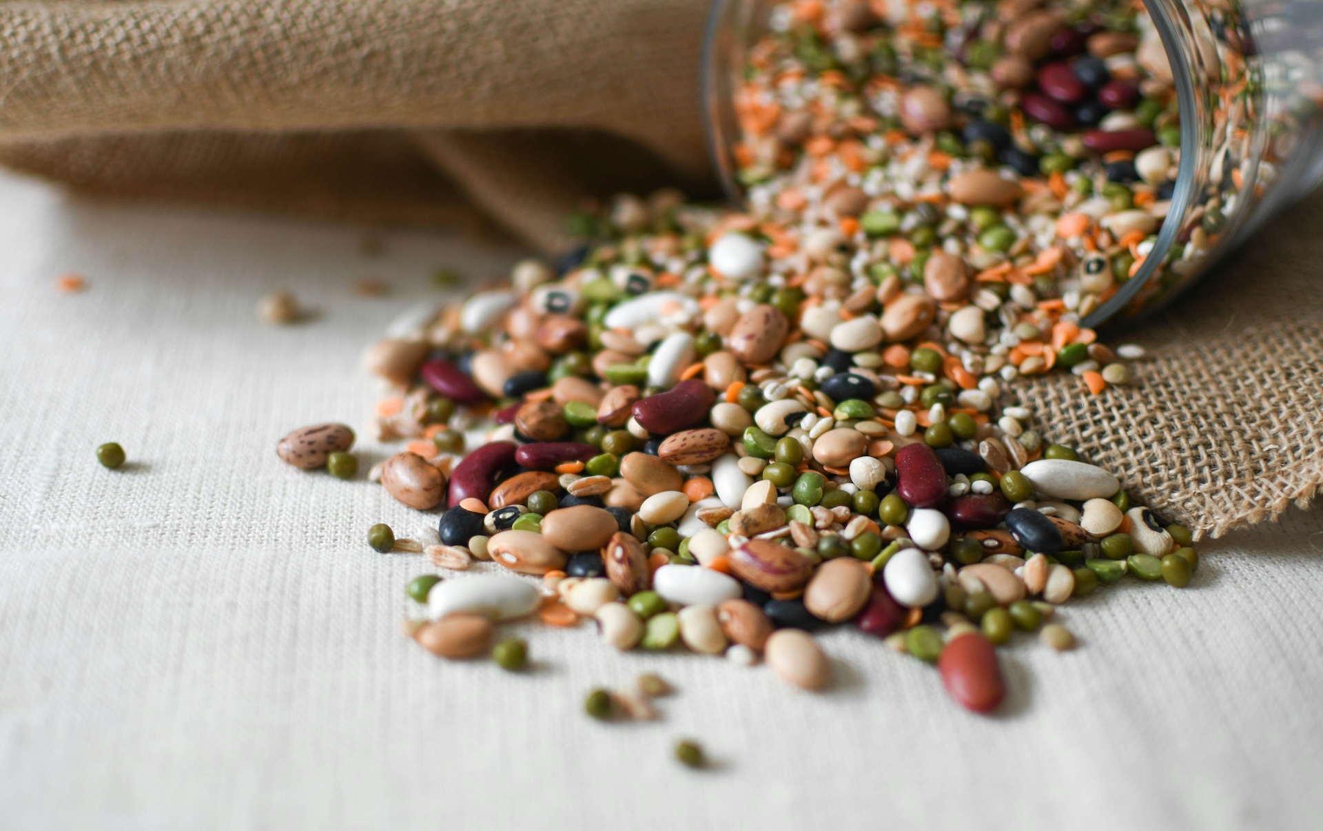 Mixed dried beans and lentils spilling from a glass jar, examples of high protein high fiber foods