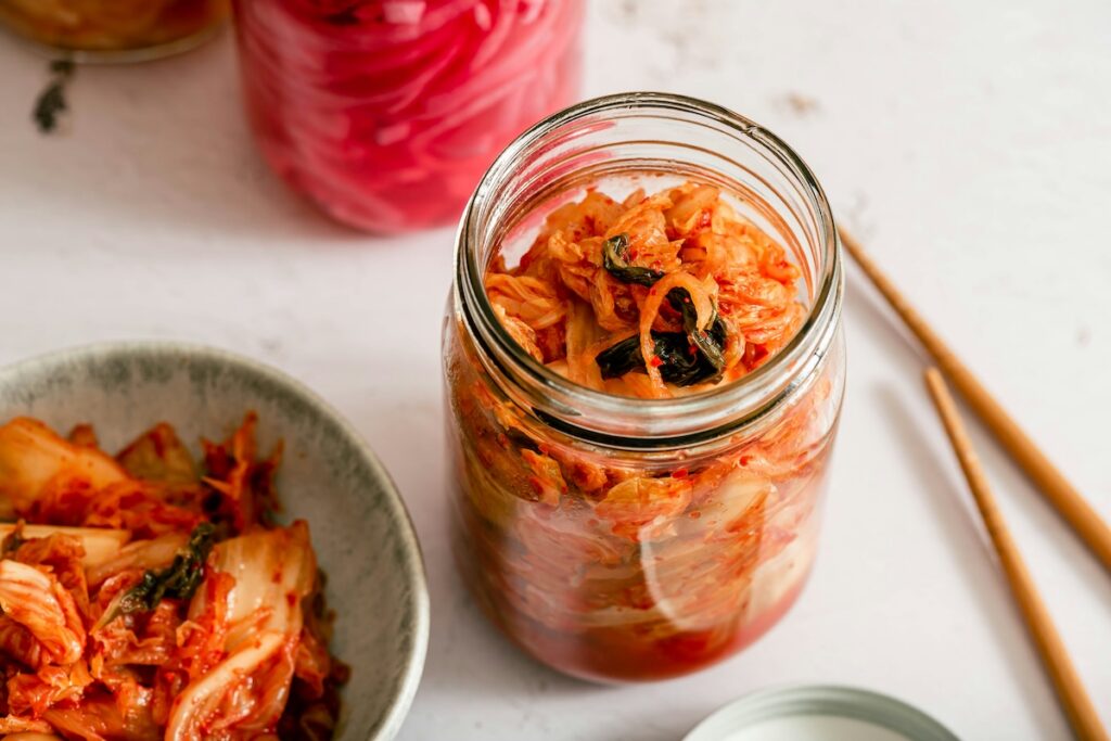 Jar of kimchi, a fermented food for gut health, alongside a bowl of kimchi and pickled radish