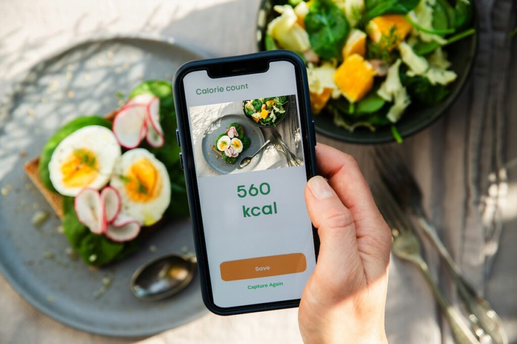 phone showing a 560 kcal calorie count app next to a low calorie lunch ideas plate of eggs and salad