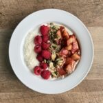 Overhead view of a peach compote yogurt bowl with Greek yogurt, raspberries, shredded coconut, and pumpkin seeds on a white plate.