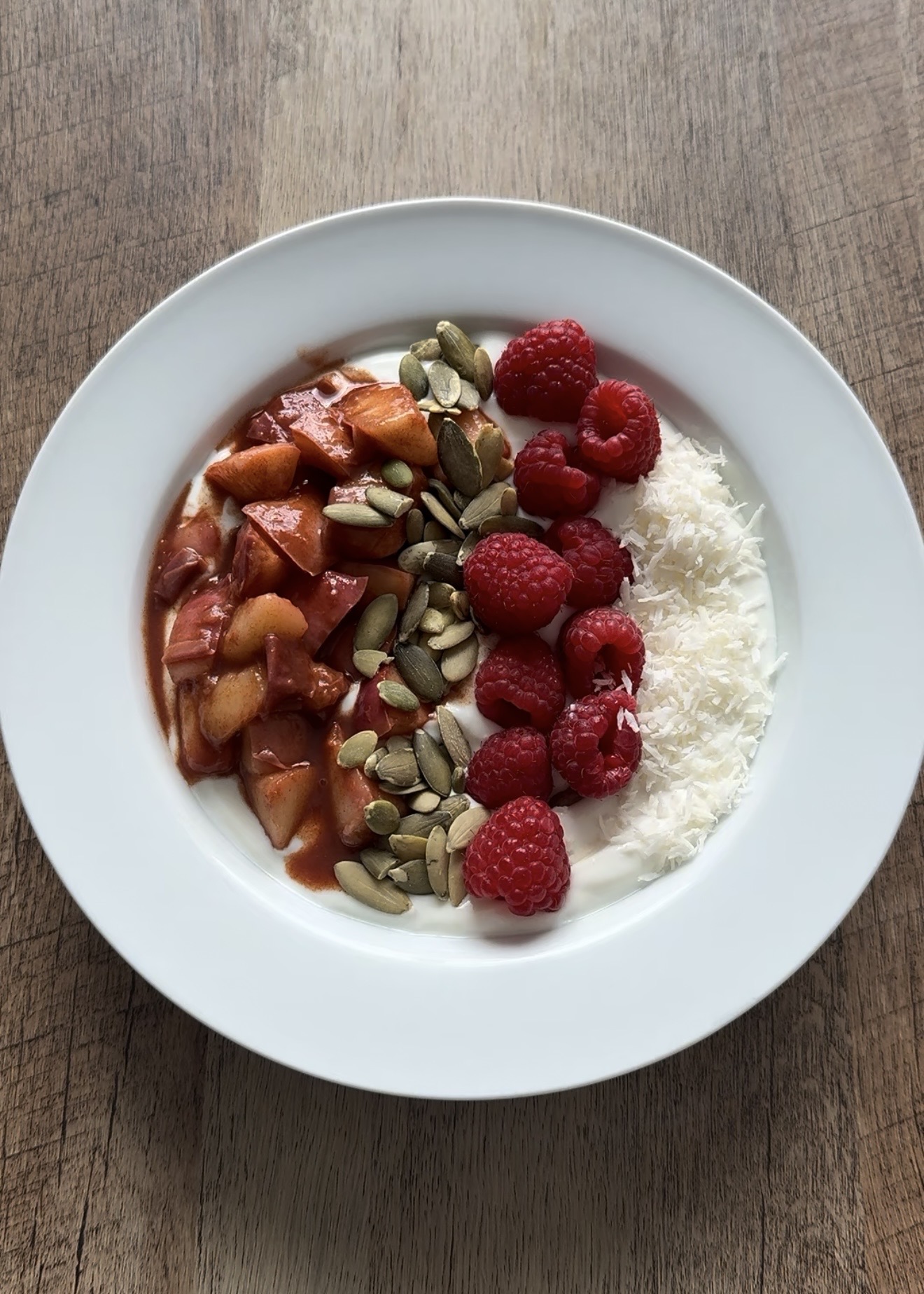 Finished peach compote yogurt bowl topped with pumpkin seeds, fresh raspberries, and shredded coconut.
