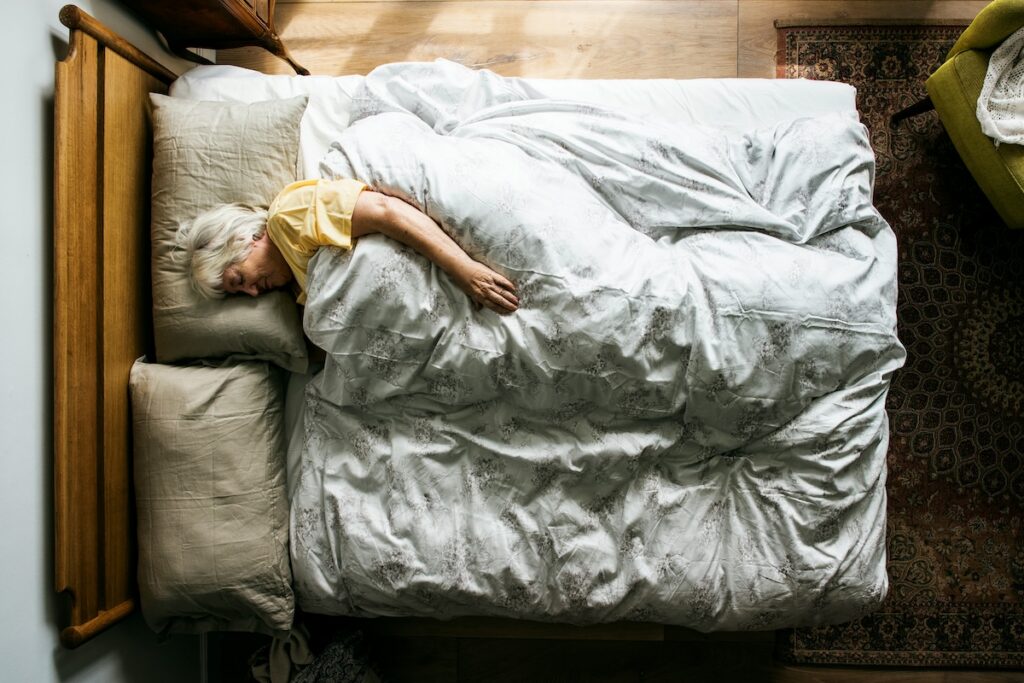 Older woman sleeping on her side in bed — pillow height and eye pressure is a key factor for older adults at higher risk of glaucoma