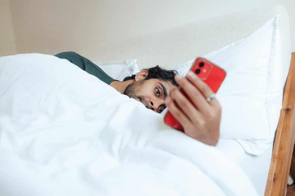 Man in bed scrolling on his phone at night, a screen habit to avoid when working on sleep without melatonin.