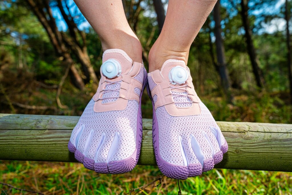 Person balancing on a wooden beam wearing zero-drop toe shoes with a wide toe box, demonstrating footwear that supports foot strengthening exercises