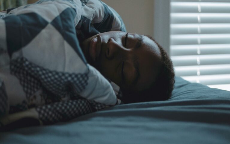Person sleeping under a patterned blanket in bed.