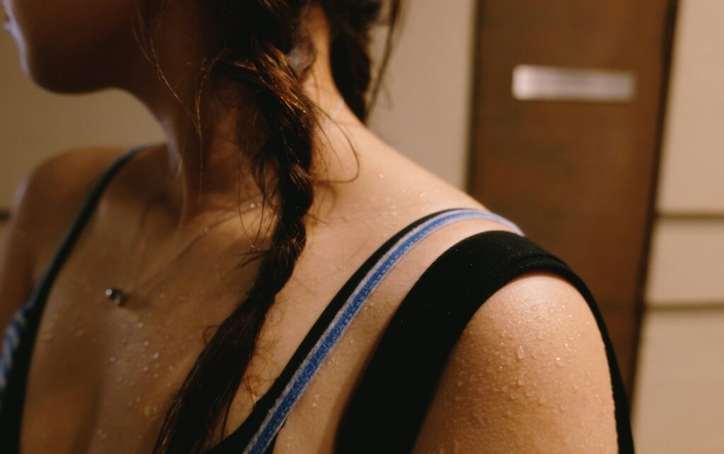 Close-up of sweat droplets on a woman's shoulder and collarbone after a workout, showing what your sweat can tell you about your health.