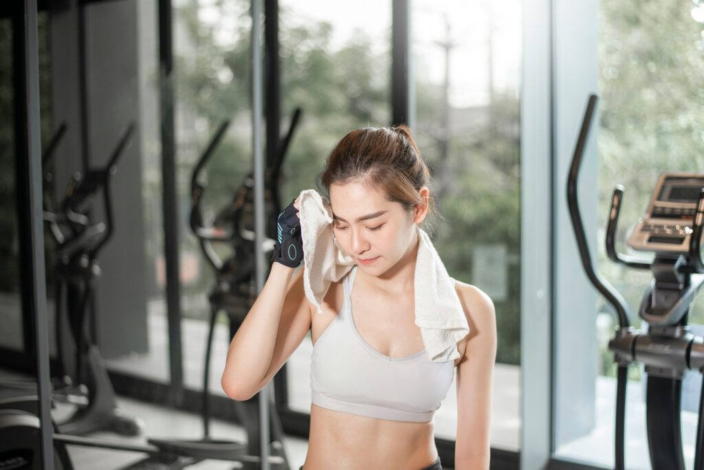 Woman wiping sweat from her face with a towel after an intense gym workout, a reminder of what your sweat can tell you about hydration and electrolyte loss.