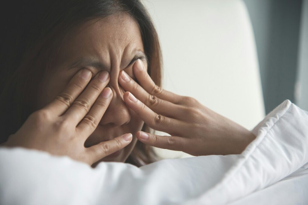 A tired woman rubs her eyes in bed after a poor night's rest, a common struggle with ADHD and sleep.