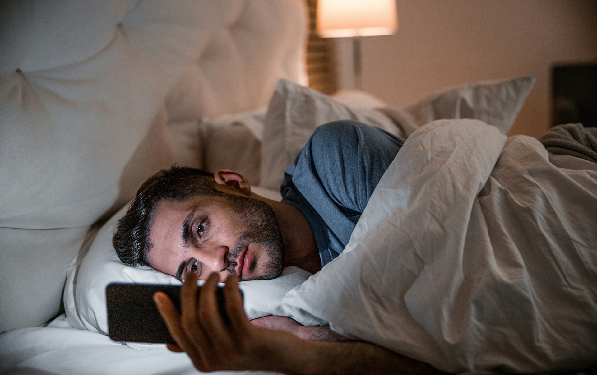 A man lies awake in bed scrolling on his phone late at night, a common pattern in ADHD and sleep problems.