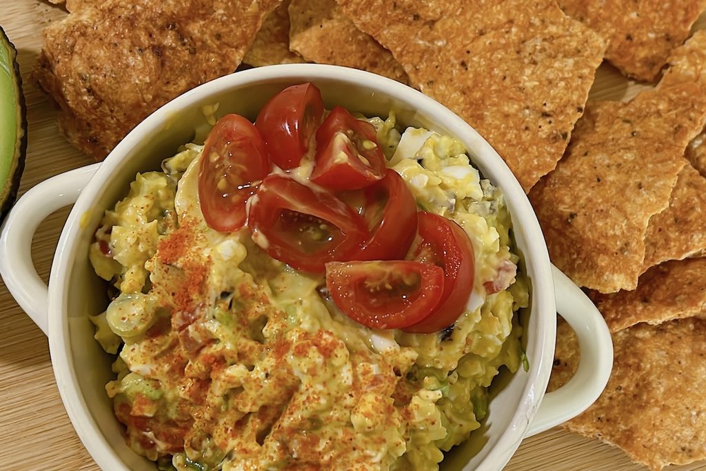 Avocado egg salad topped with cherry tomatoes and paprika, served with crispy chicken chips, one of six high protein meals.