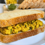 Vegan egg salad sandwich on crusty bread with smashed turmeric tofu and chives, a high-protein meal prep lunch