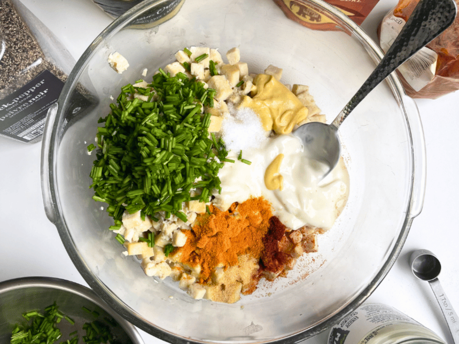 Vegan egg salad ingredients in a glass bowl: tofu cubes, chives, vegan mayo, dijon, turmeric, and smoked paprika