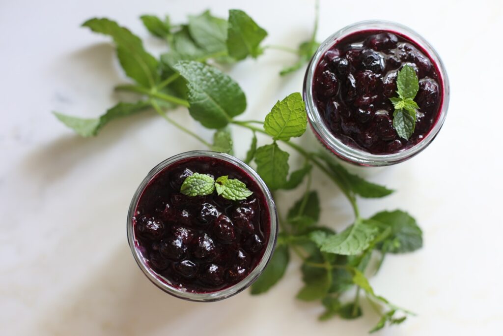 High protein meal prep idea: two jars of blueberry compote topped with fresh mint for Greek yogurt parfaits