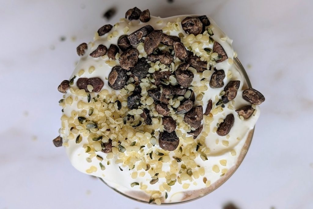Overhead view of a chocolate shake smoothie topped with whipped cream, cacao nibs, and hemp seeds, a sweet option among high protein meals.