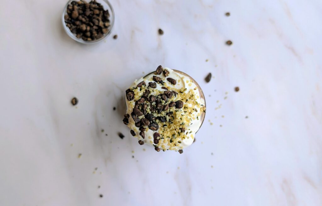 Chocolate smoothie topped with whipped cream, cacao nibs, and hemp seeds, seen from above