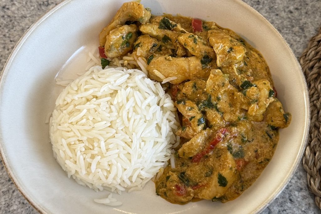 Creamy turmeric chicken with red peppers and fresh herbs served beside fluffy white rice, an easy dinner for high protein meals.