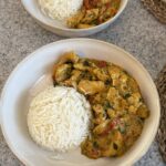 Creamy turmeric chicken with red bell peppers and parsley served beside white rice in a bowl