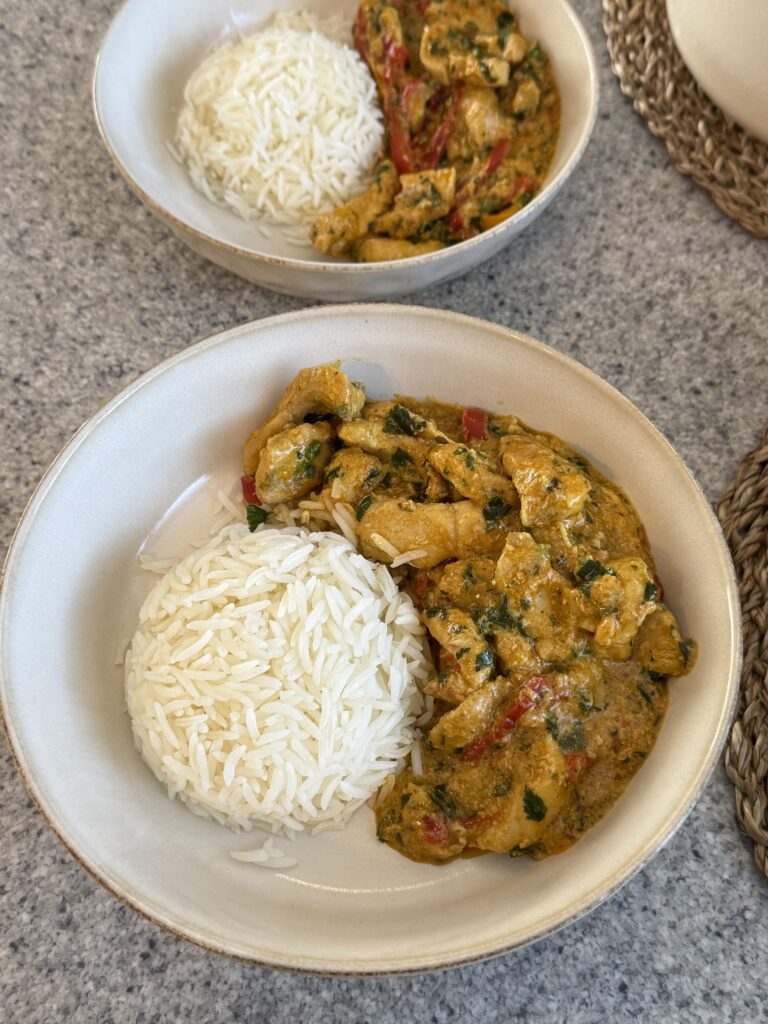 Creamy turmeric chicken with red bell peppers and parsley served beside white rice in a bowl