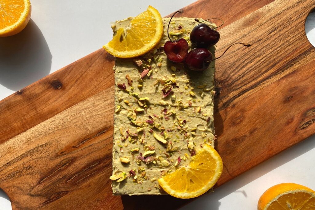 Chocolate pistachio cake covered in pistachio yogurt cream and chopped pistachios, garnished with orange slices and cherries for simple healthy meals