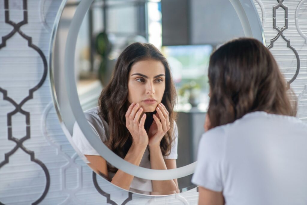 What does collagen do? A woman touches her face and checks her skin in the mirror, wondering if collagen supplements really work.
