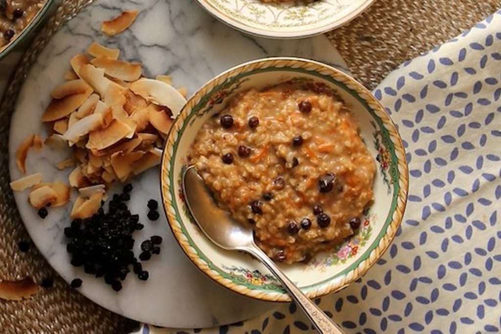 Bowl of morning glory oats with shredded carrot and currants beside toasted coconut flakes, a hearty breakfast in this week’s high protein meals.