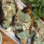 Roasted cabbage wedges with charred edges, topped with herby green sauce and toasted sliced almonds on a platter