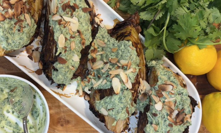 Roasted cabbage wedges with charred edges, topped with herby green sauce and toasted sliced almonds on a platter