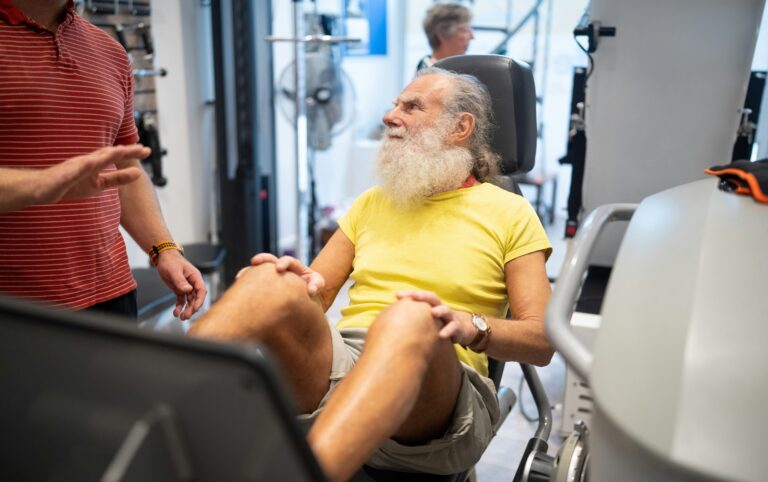 Older man on a leg press machine talking with a trainer, training to fight age-related muscle loss