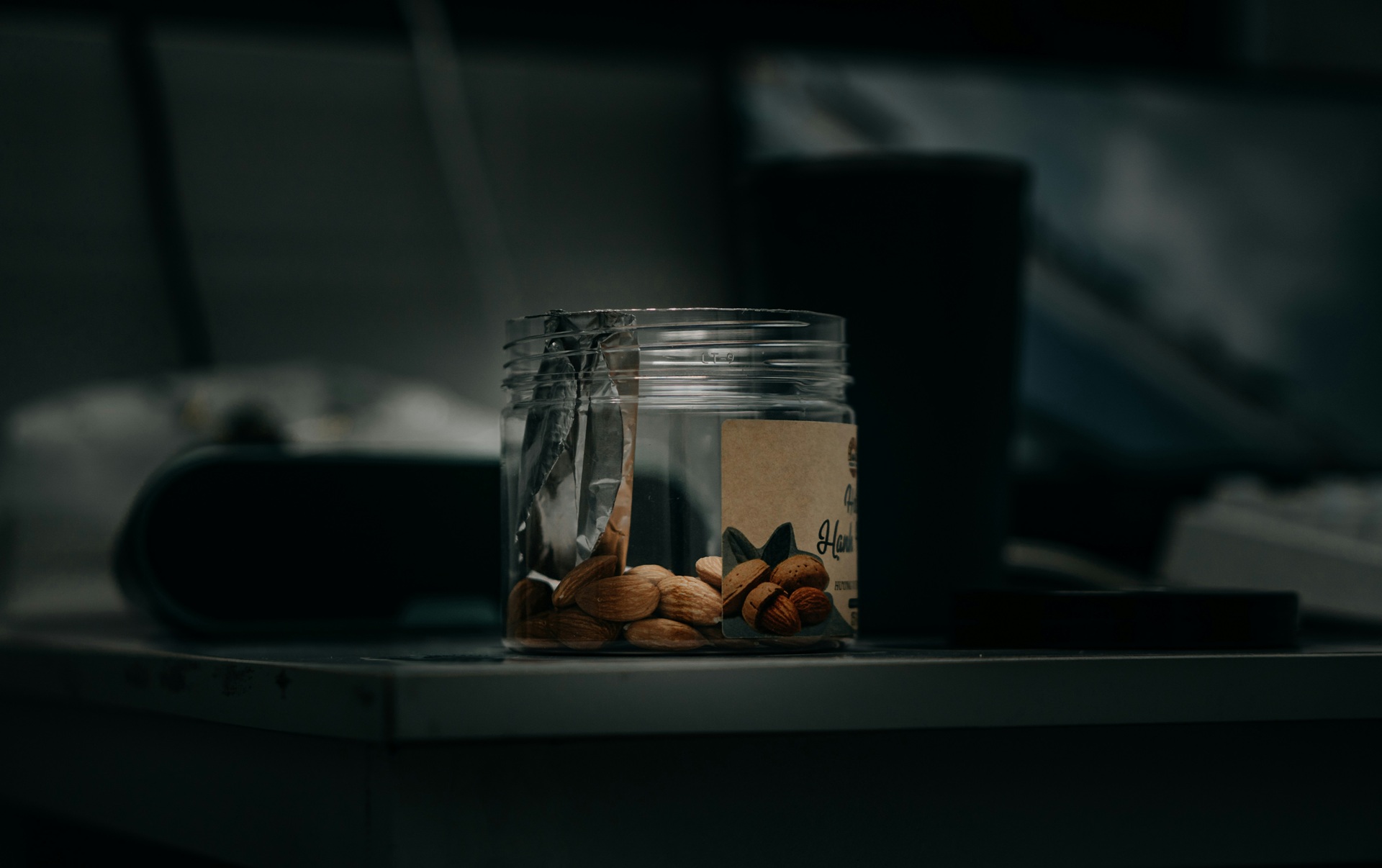 Small clear jar of whole almonds on a dimly lit bedside table at night, a simple evening snack linked to research on almonds for sleep
