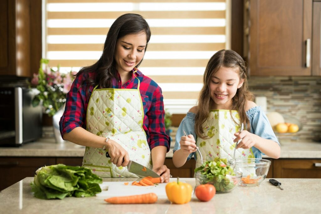 Woman and girl chopping carrots and tossing a salad as part of the best food for blood pressure.