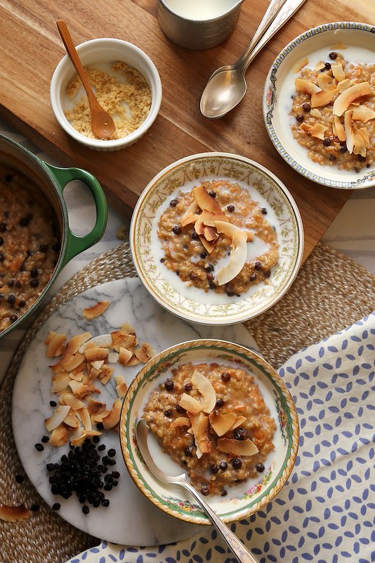 Three bowls of morning glory oats topped with toasted coconut flakes and currants, served with milk and brown sugar