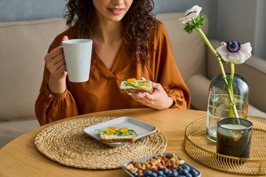 Woman enjoying toast with cream cheese, arugula, and tomatoes with a cup of coffee, one of many easy healthy breakfast ideas