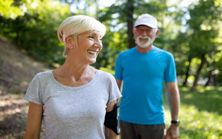 Smiling older couple walking outdoors in a sunny park, showing how regular exercise can lower risk of death, heart disease, and dementia
