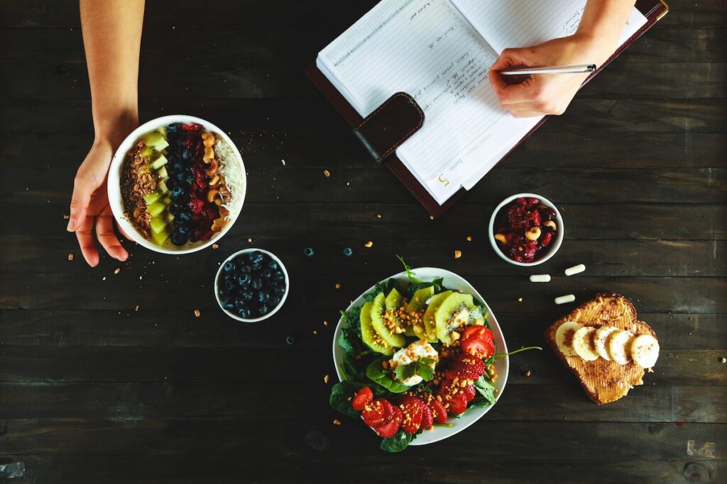 Foods that lower blood pressure, including a spinach and berry salad, blueberries, and banana toast, beside a meal planner