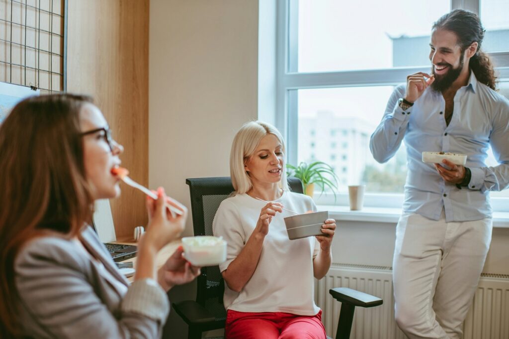Coworkers sharing healthy snacks for work and chatting during a break in the office