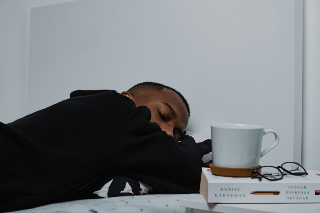 Man asleep face-down on his pillow next to a mug on the nightstand, a reminder that watching late caffeine is part of how to get more deep sleep