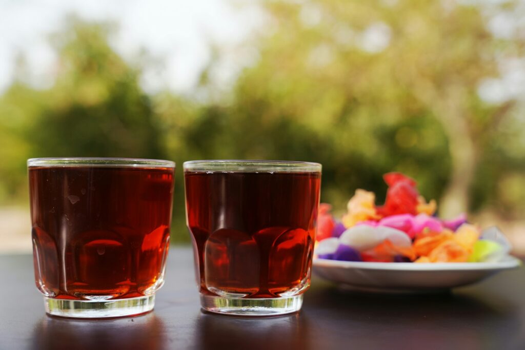 Two glasses of red drink beside a plate of colorful candies, common sources of Red 40 and the question of whether it is bad for you