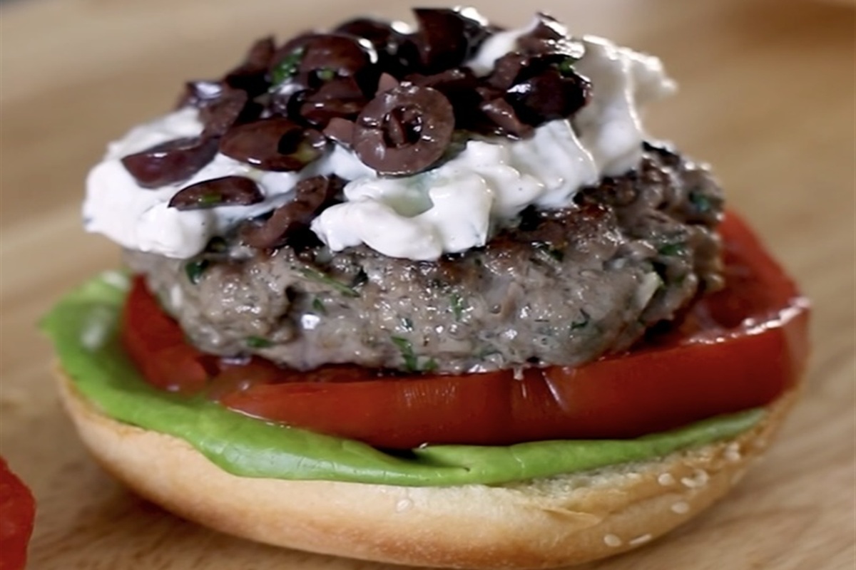 High protein meal prep idea: open-faced lamb burger with tzatziki, olives, tomato, and lettuce on a sesame bun