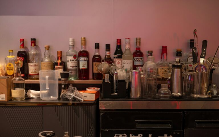 Bar shelf lined with liquor bottles, cocktail shakers, and glasses, the makings of the least healthy alcoholic drinks