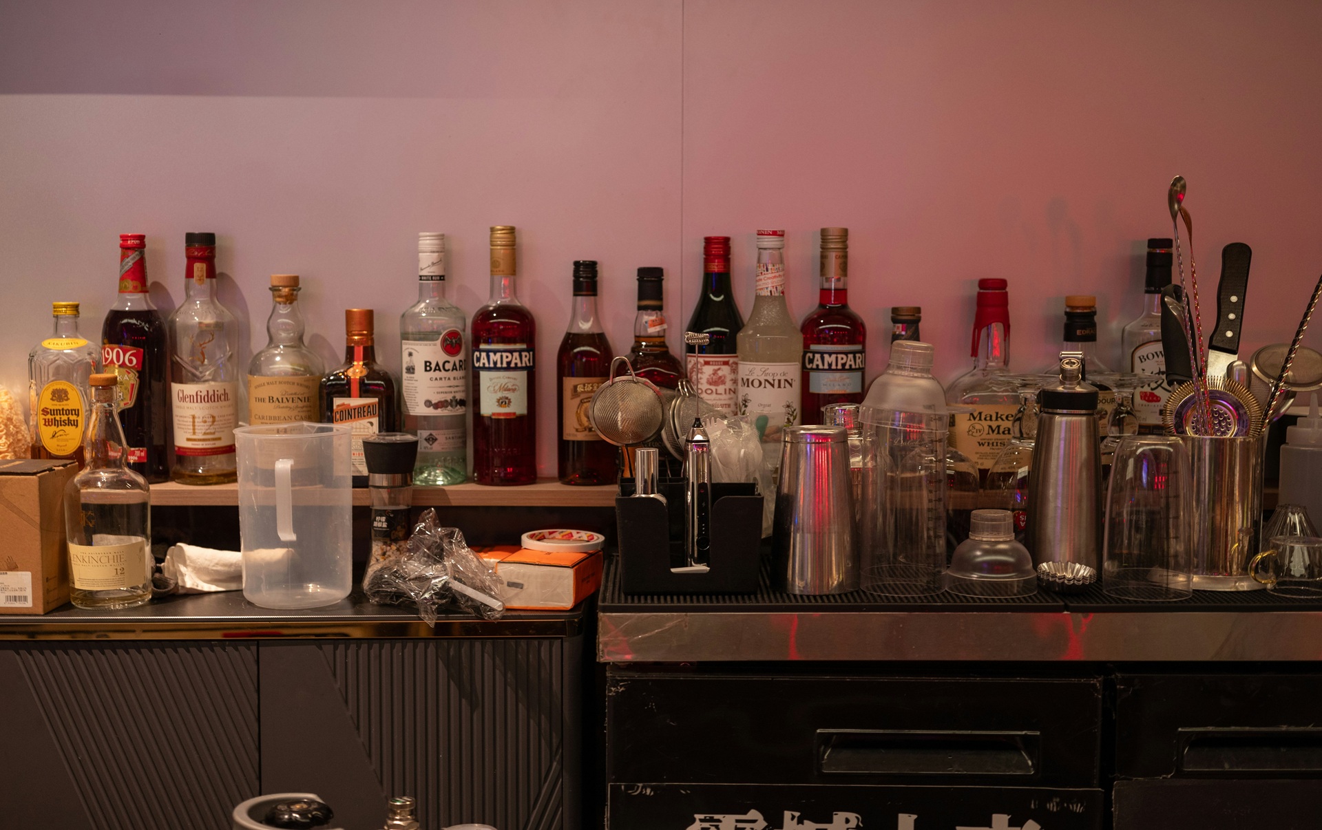 Bar shelf lined with liquor bottles, cocktail shakers, and glasses, the makings of the least healthy alcoholic drinks