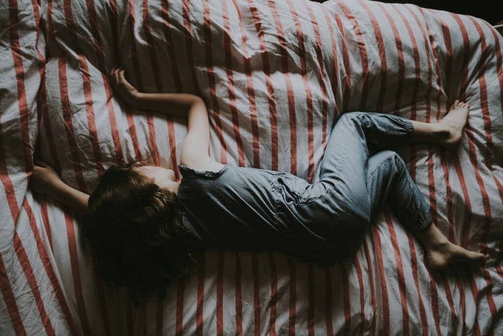Person lying curled up on a striped bed, trying to fall asleep using the military sleep method