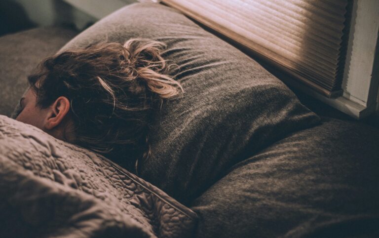 Woman sleeping soundly under a blanket in a dimly lit bedroom after using the military sleep method