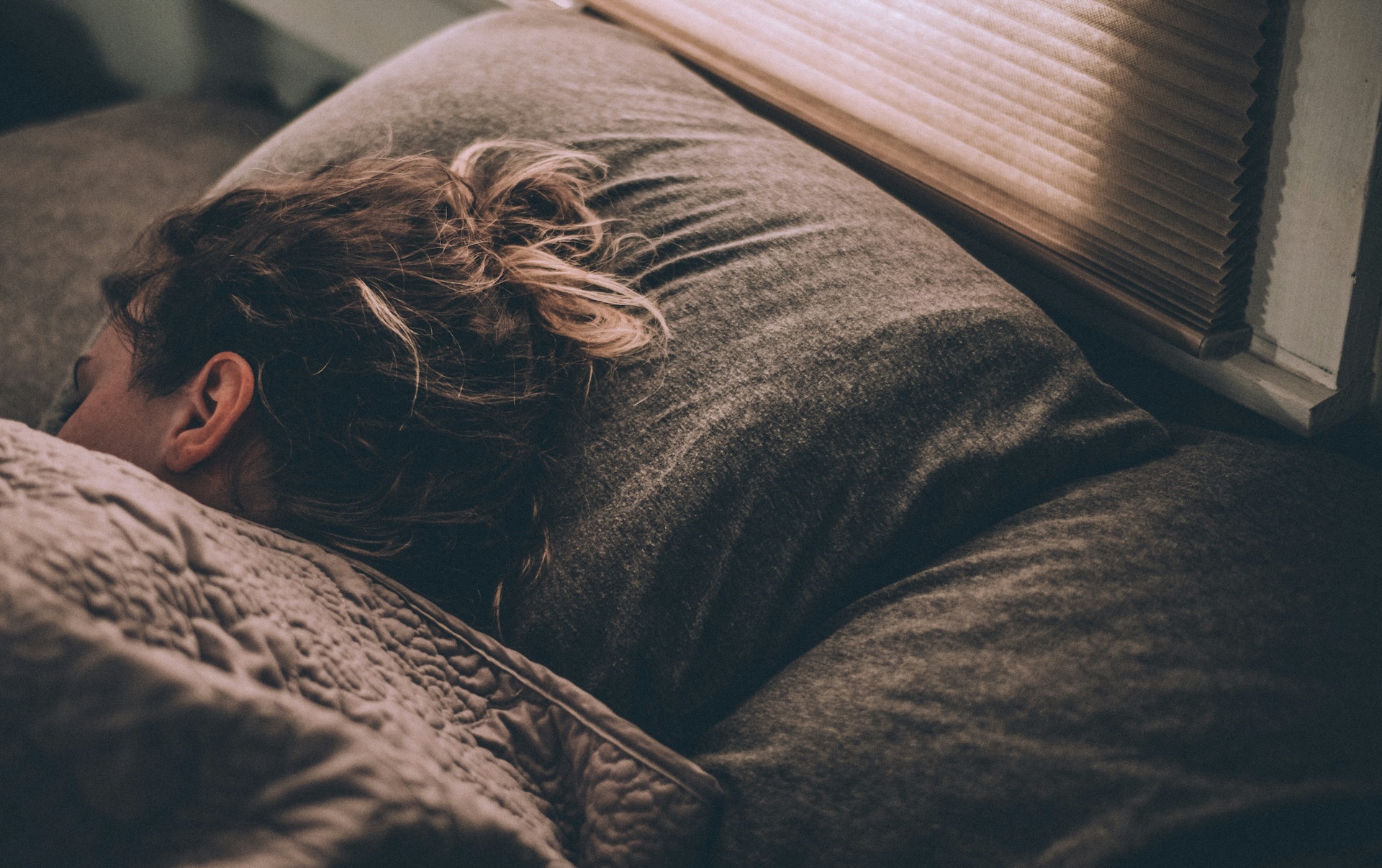 Woman sleeping soundly under a blanket in a dimly lit bedroom after using the military sleep method