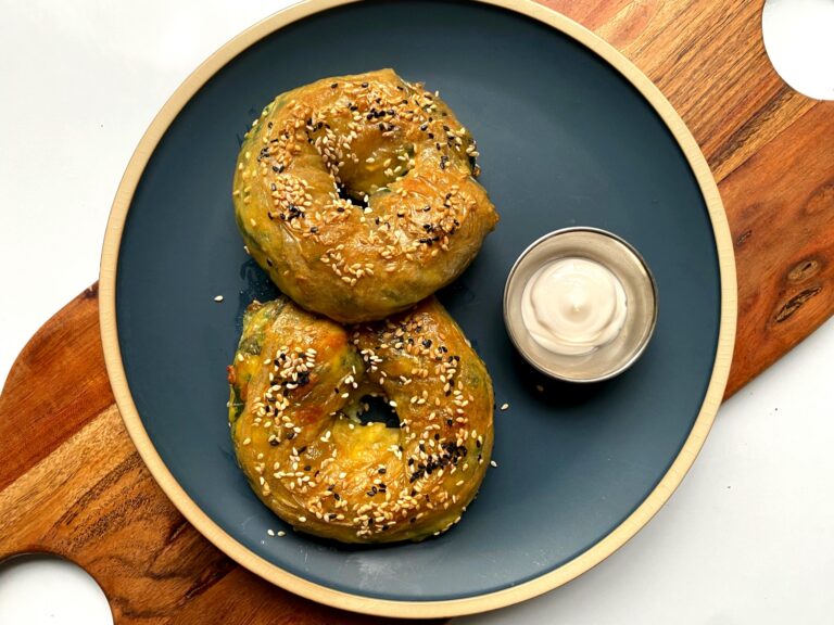 Two golden rice paper bagels topped with sesame seeds on a plate with a small bowl of dip