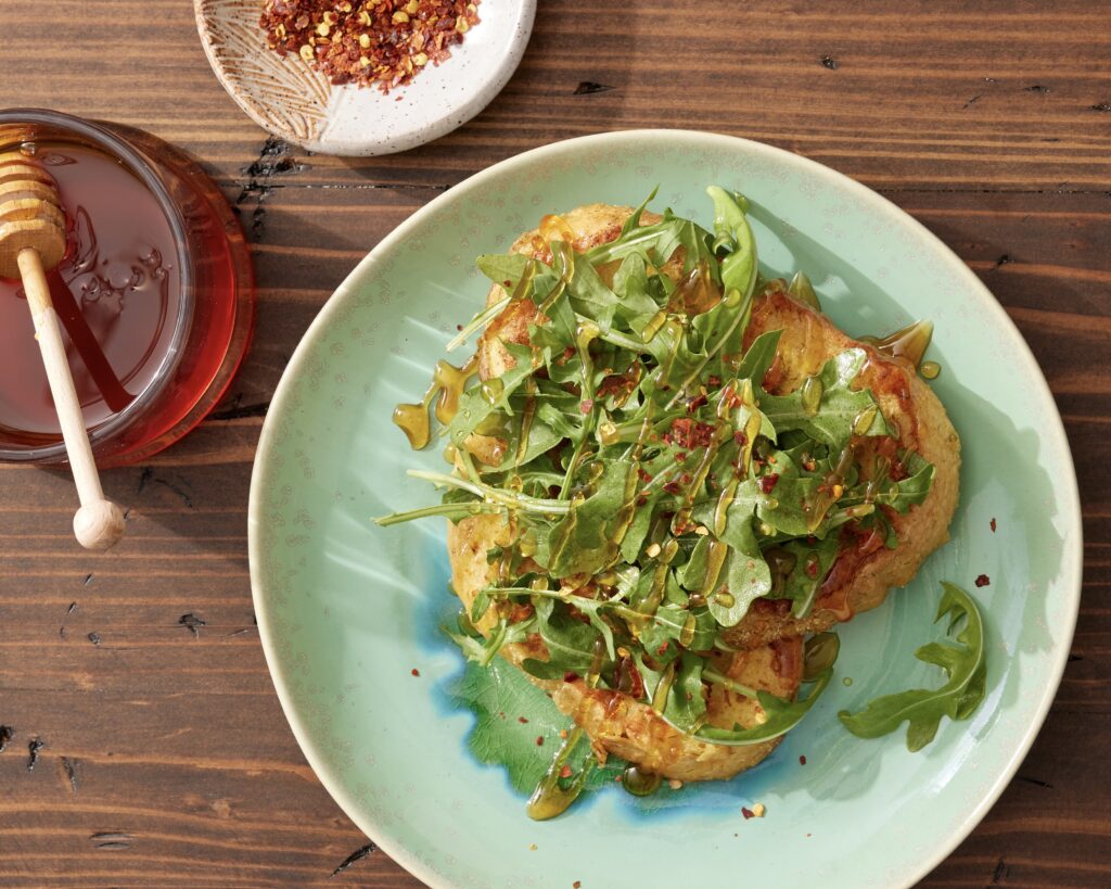 Savory french toast topped with arugula, a honey drizzle, and red pepper flakes on a green plate