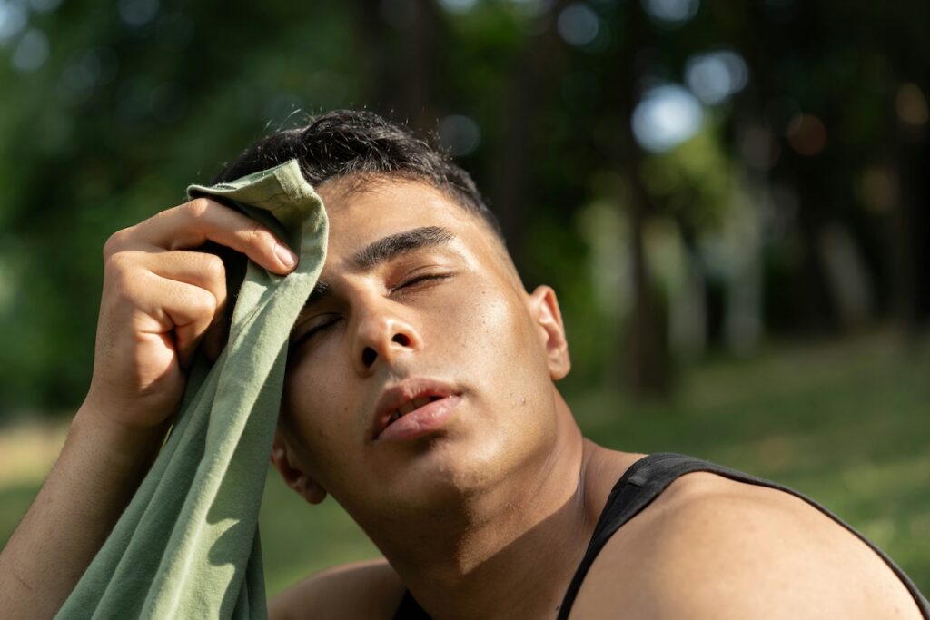 Man wiping sweat from his forehead outdoors, showing one of the signs and symptoms of dehydration