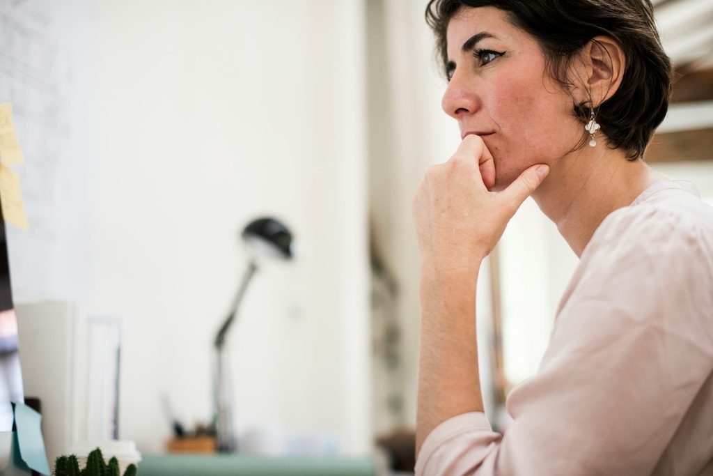 Woman with short dark hair resting her chin on her hand, thinking about the signs of perimenopause