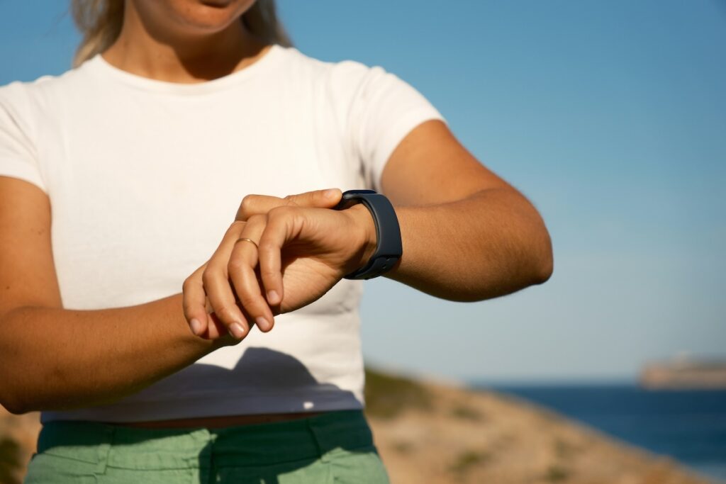 Woman checking her fitness watch during an outdoor workout by the sea, a reminder that cardio and strength training work together for heart health
