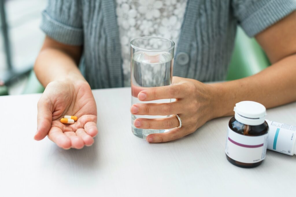 Instead of taking supplements with coffee, a woman holds two capsules and a glass of water beside supplement bottles
