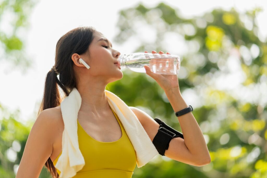 Woman drinking water outdoors after a workout, a way to prevent the signs and symptoms of dehydration